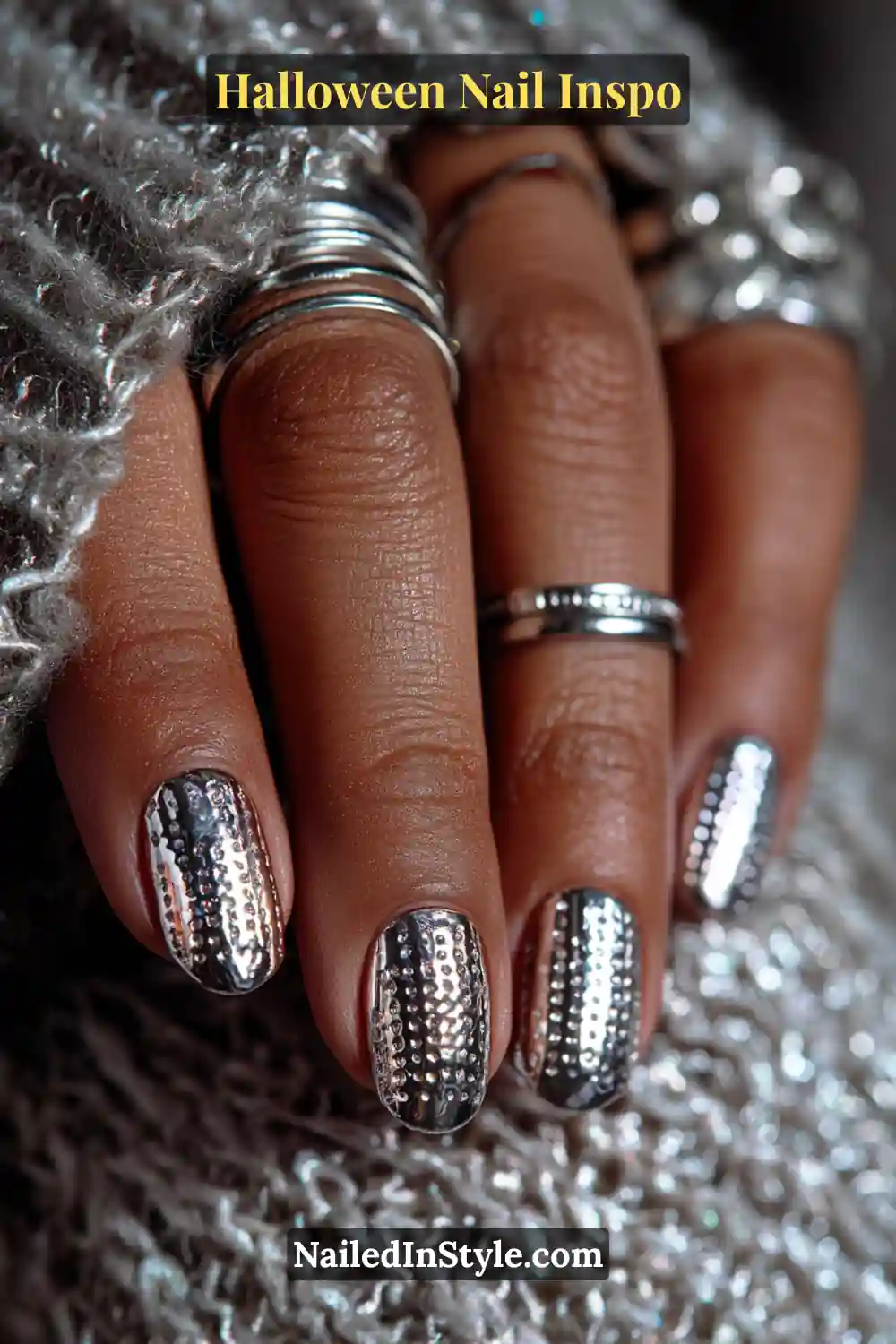 Short squoval nails with a glossy graphite base detailed with tiny silver chrome pin-dots along the cuff, styled with stainless steel rings for a futuristic Halloween look.