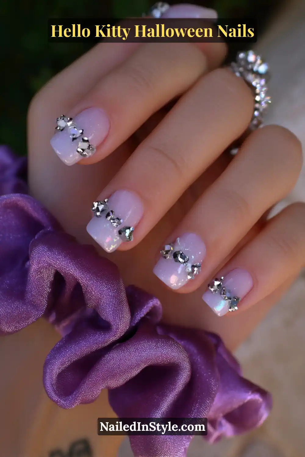 Short squoval nails with a translucent lavender-rose base, embellished with crystal confetti clusters near the tips for a 3D sparkle effect. Styled with a pink satin scrunchie for a playful yet elegant Hello Kitty Halloween aesthetic.