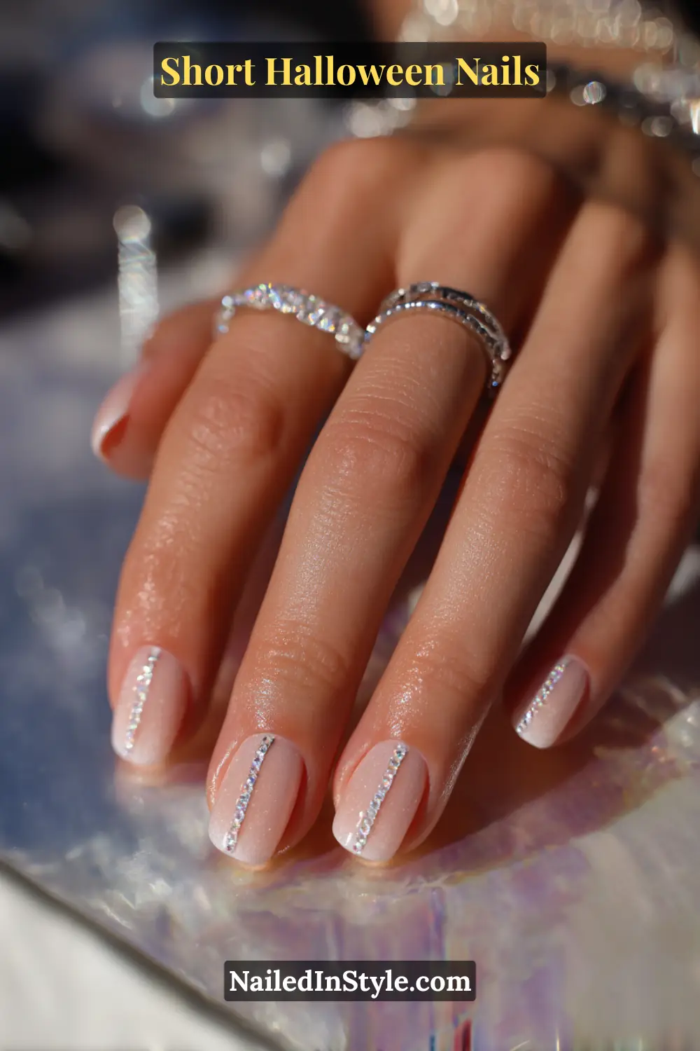 Short squoval nails with five micro crystals forming a vertical dewline down the center, minimalist jeweled finish; styled with sparkling silver rings and iridescent background, refined short Halloween nails for all skin tones.
