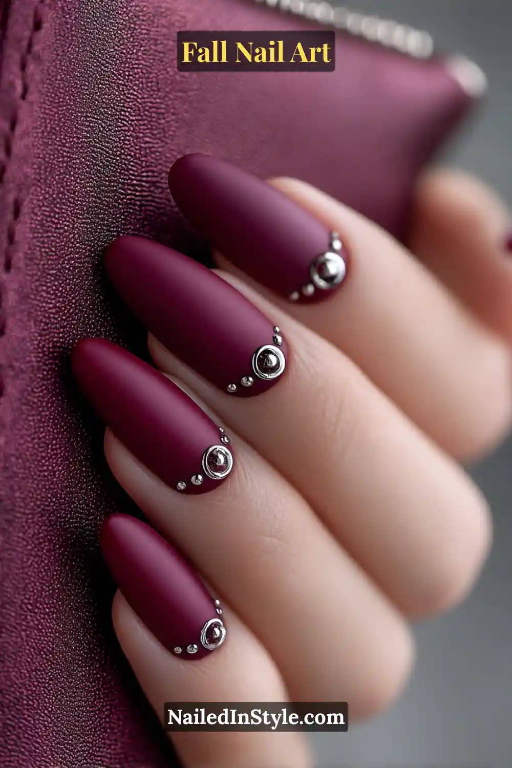 Medium coffin nails in rich fig matte polish, accented with small 3D chrome buttons near the cuticle in gunmetal tones, creating a plush yet edgy metallic contrast.
