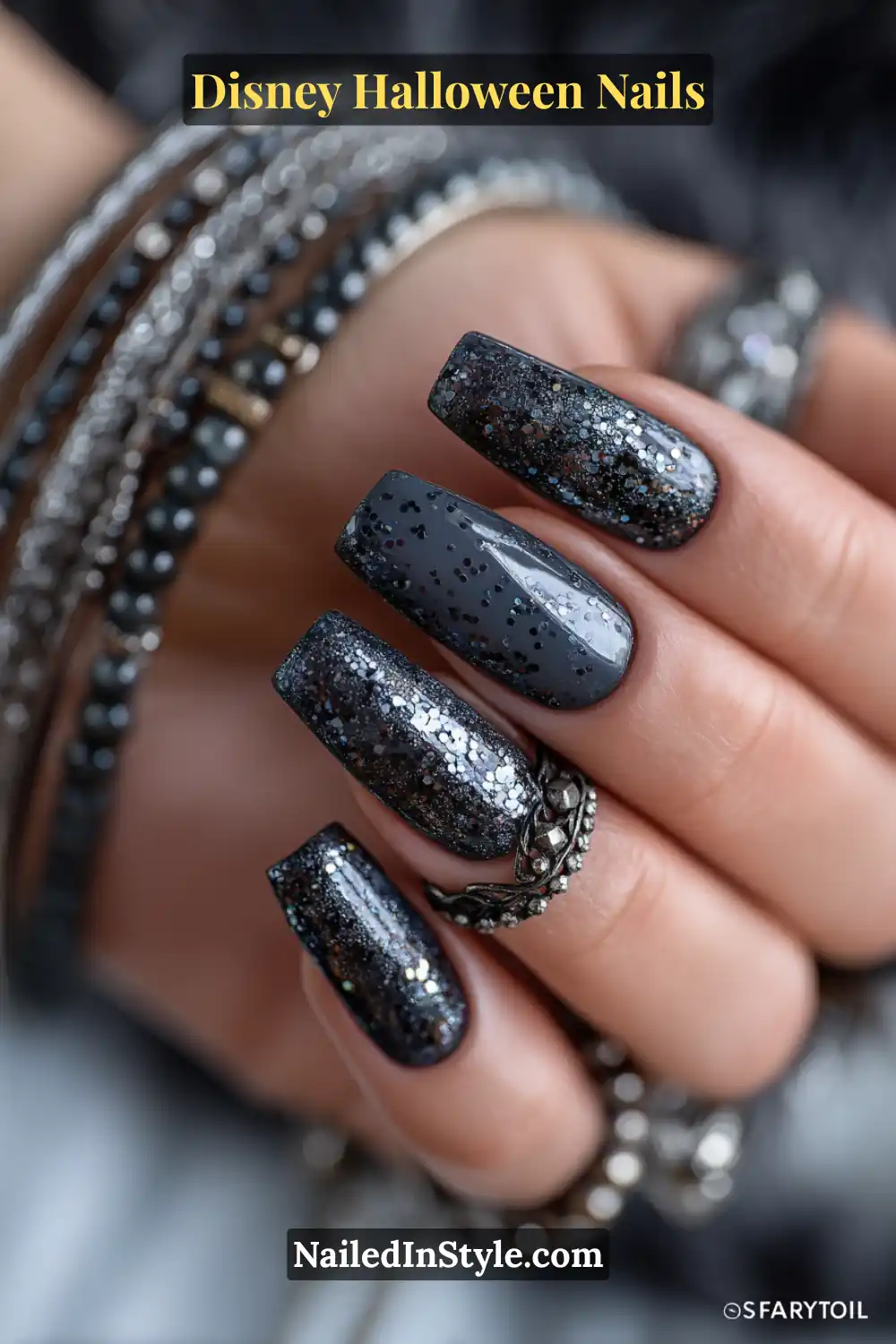 Long soft coffin nails in deep graphite with shimmering mirror-chrome dots scattered like fireflies across accent nails; paired with stacked silver bangles for a glowing Disney Halloween vibe.