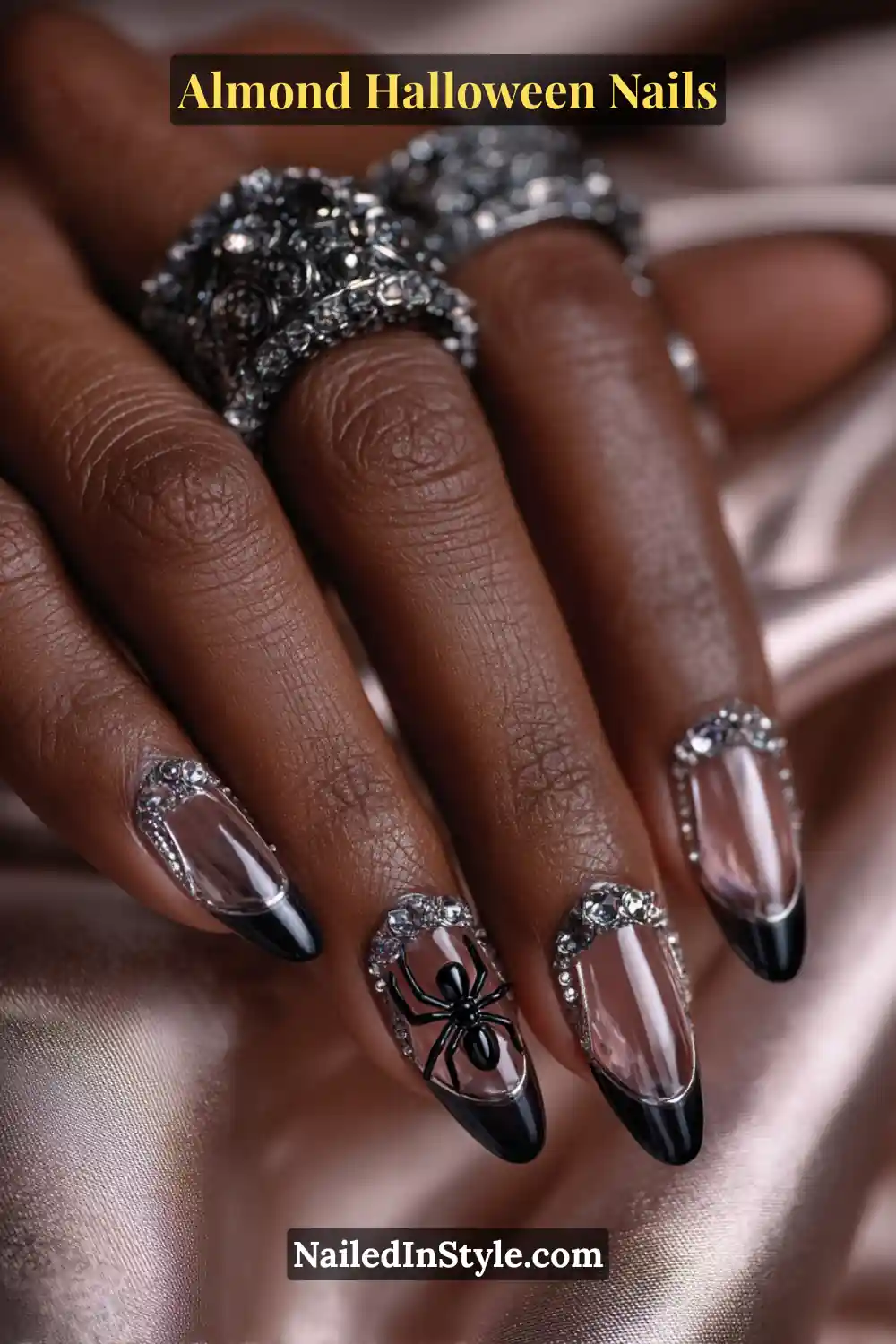 Close-up almond nails with clear acrylic base featuring a suspended 3D black spider charm and crystal accents near the cuticle, glossy encapsulated finish, Almond Halloween Nails.
