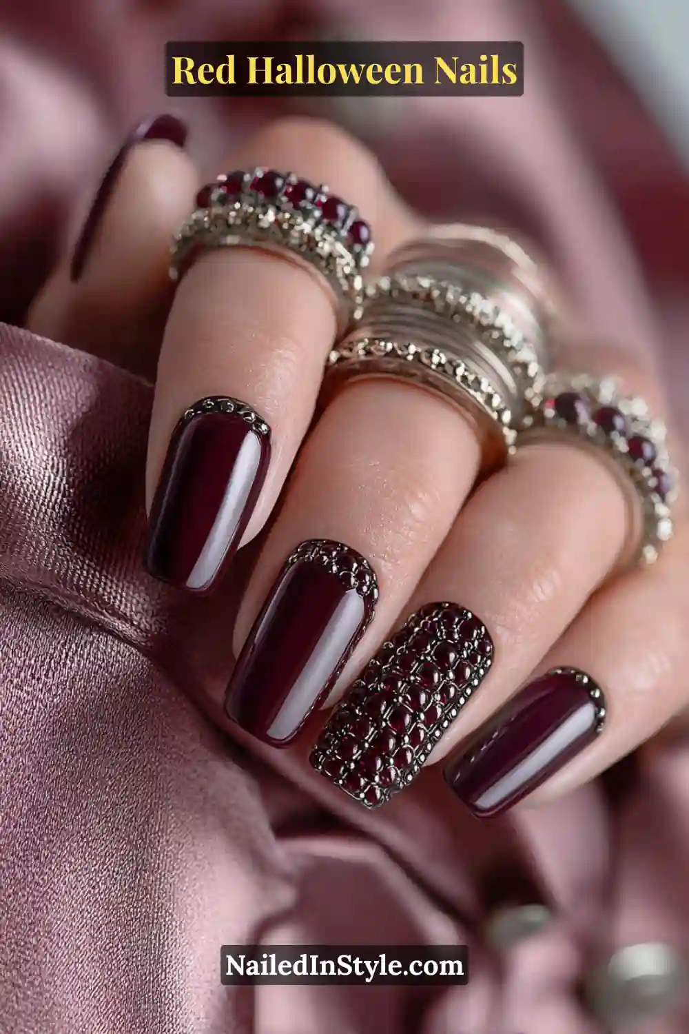 Long ballerina nails painted in deep garnet red with micro hematite studs forming a thin lattice cuff; paired with stacked metallic bangles; luxurious 3D nail look flattering for all skin tones under moody lighting.