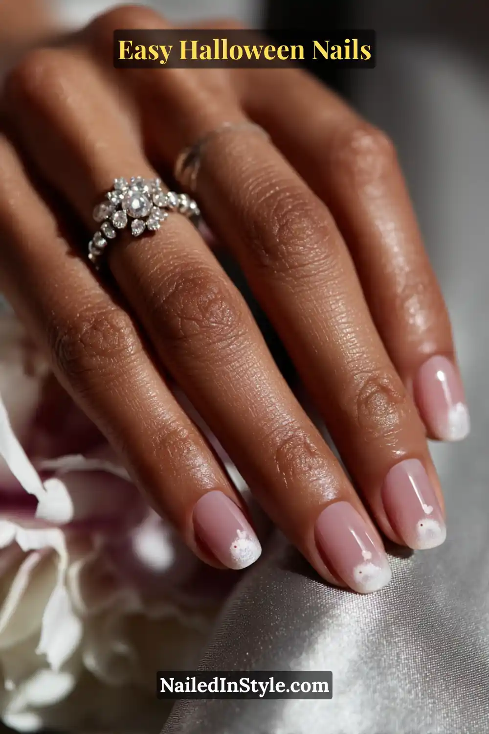 Short oval nails painted in a sheer pink base with a tiny white ghost puff and two delicate eyes on one accent nail, finished with a soft veil gloss for Easy Halloween Nails.