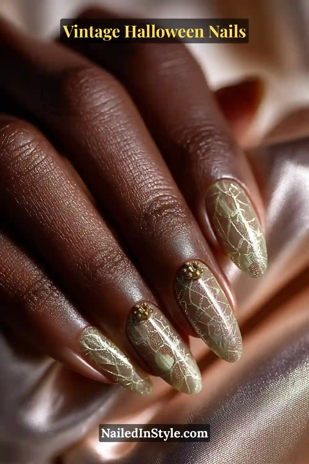 Long almond nails with a cream base detailed by fine gold cobweb lines and a small raised cameo bead accent, exuding vintage Halloween elegance.