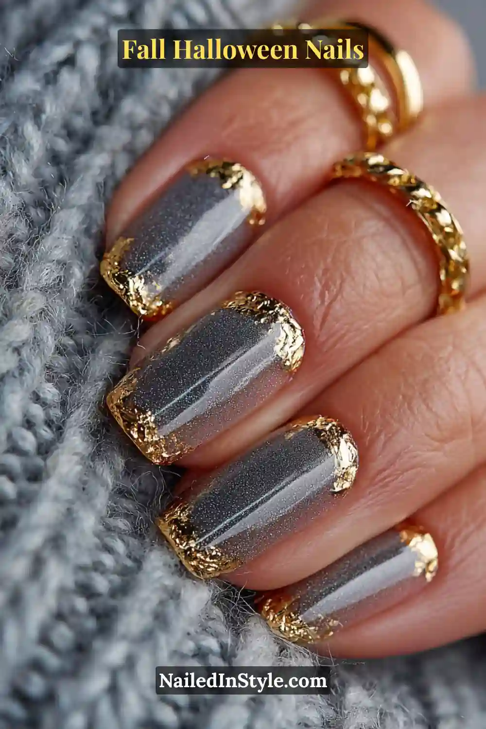 Short round nails with a sheer smoky pewter base fading into gold foil tips, paired with chunky gold rings and a soft gray knit for a rich, fall-luxury aesthetic.
