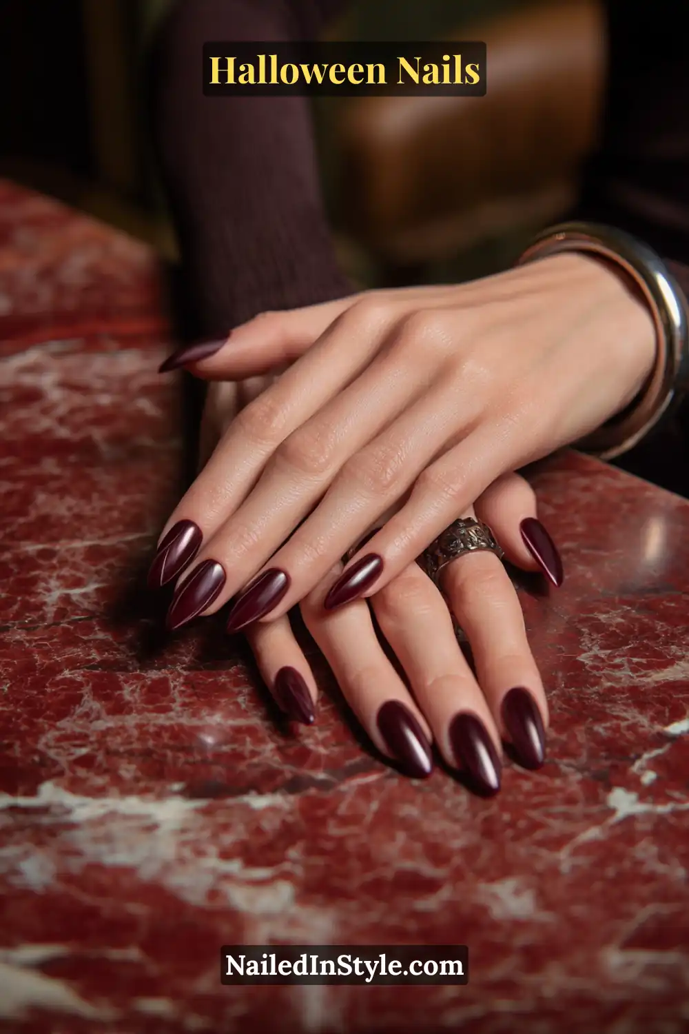 Almond and oval nails with chai-toned base detailed by ultra-thin garnet arcs sweeping from sidewall to tip, finished in glossy linework; styled with dark silver rings on a deep marbled red surface, elegant Halloween nails for fair, medium, and olive skin tones.
