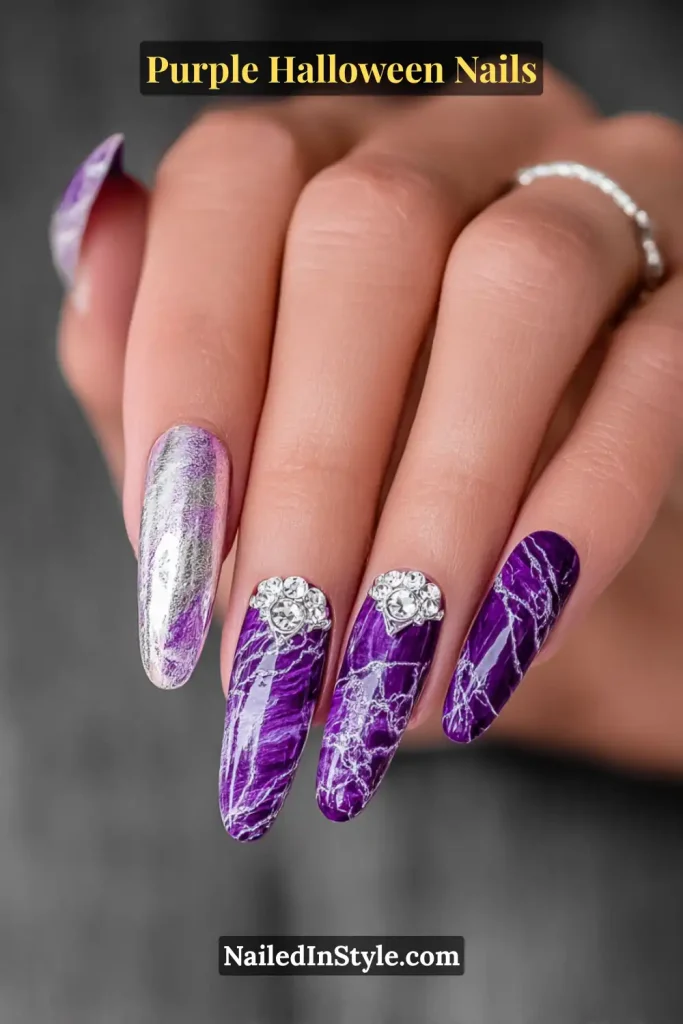 Medium almond nails in deep orchid purple with smoky silver marble veining and chrome lacing, accented by crystal embellishments that catch the light like gothic jewels.