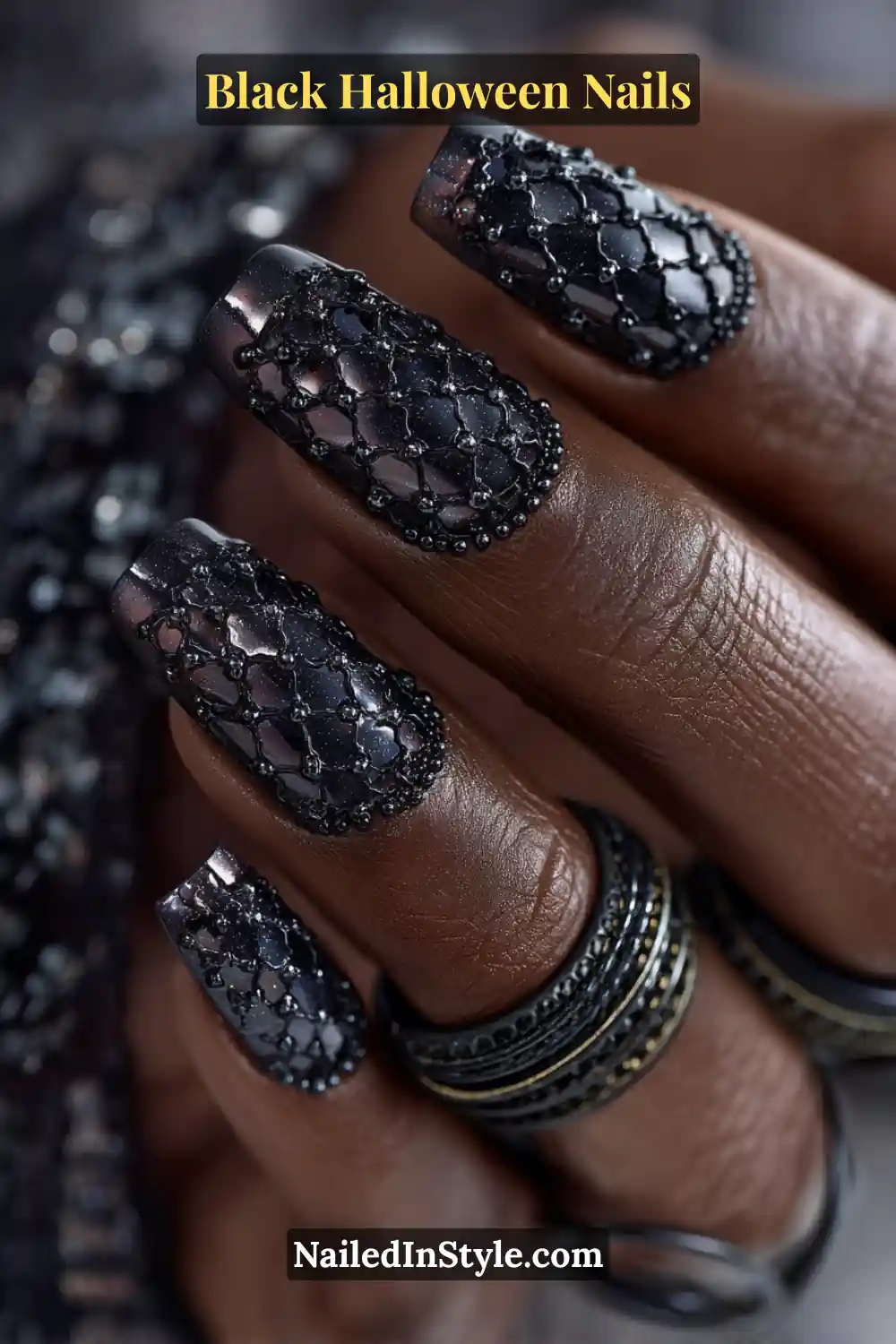 Long ballerina nails in deep graphite with hematite micro-studs arranged in a 3D lattice pattern; reflective metallic beads frame each nail; paired with stacked black and gold bangles; suits all skin tones with dimensional shine.