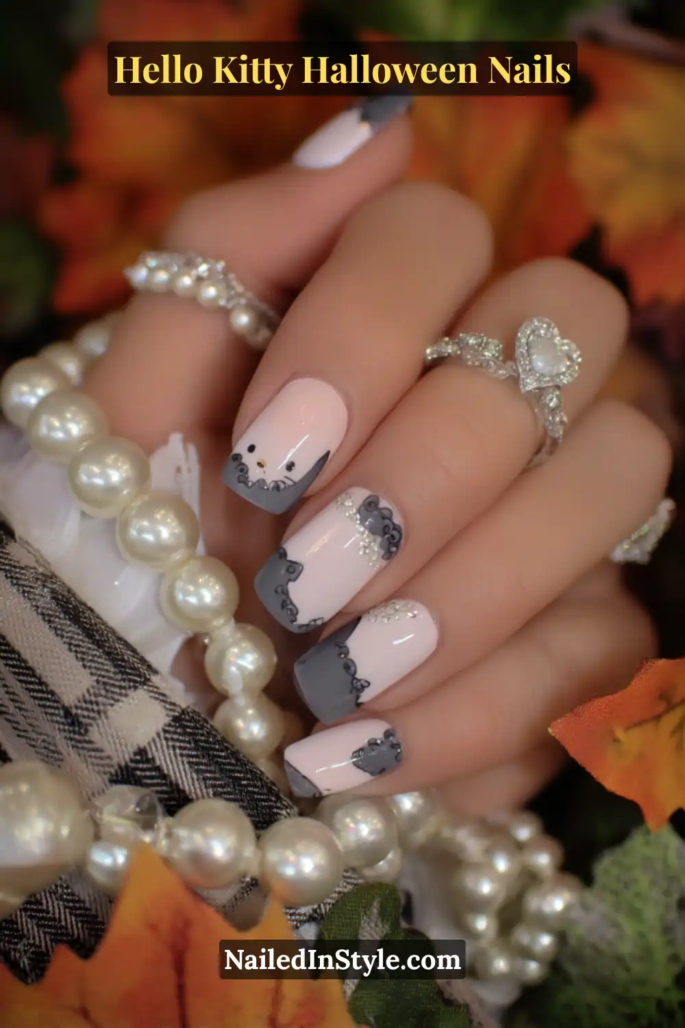 Short oval nails in porcelain pink with raised 3D Hello Kitty cameo silhouettes framed by tiny pearls and graphite lace details. The design pairs timeless charm with Halloween sophistication, styled beautifully with pearl accessories.