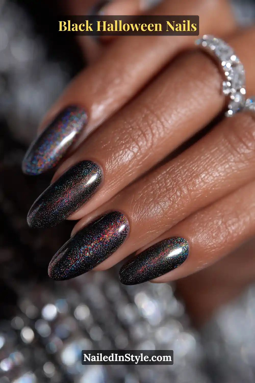 Long oval nails in sheer charcoal black with a fine holographic shimmer that reflects rainbow light; glossy finish styled with crystal jewelry for an ethereal, spectral glow.