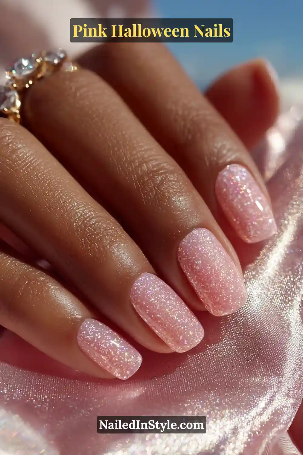 Pink Halloween nails with a petal pink holographic finish, scattered star glitter, and a glossy shimmer on short oval nails, styled with crystal rings.