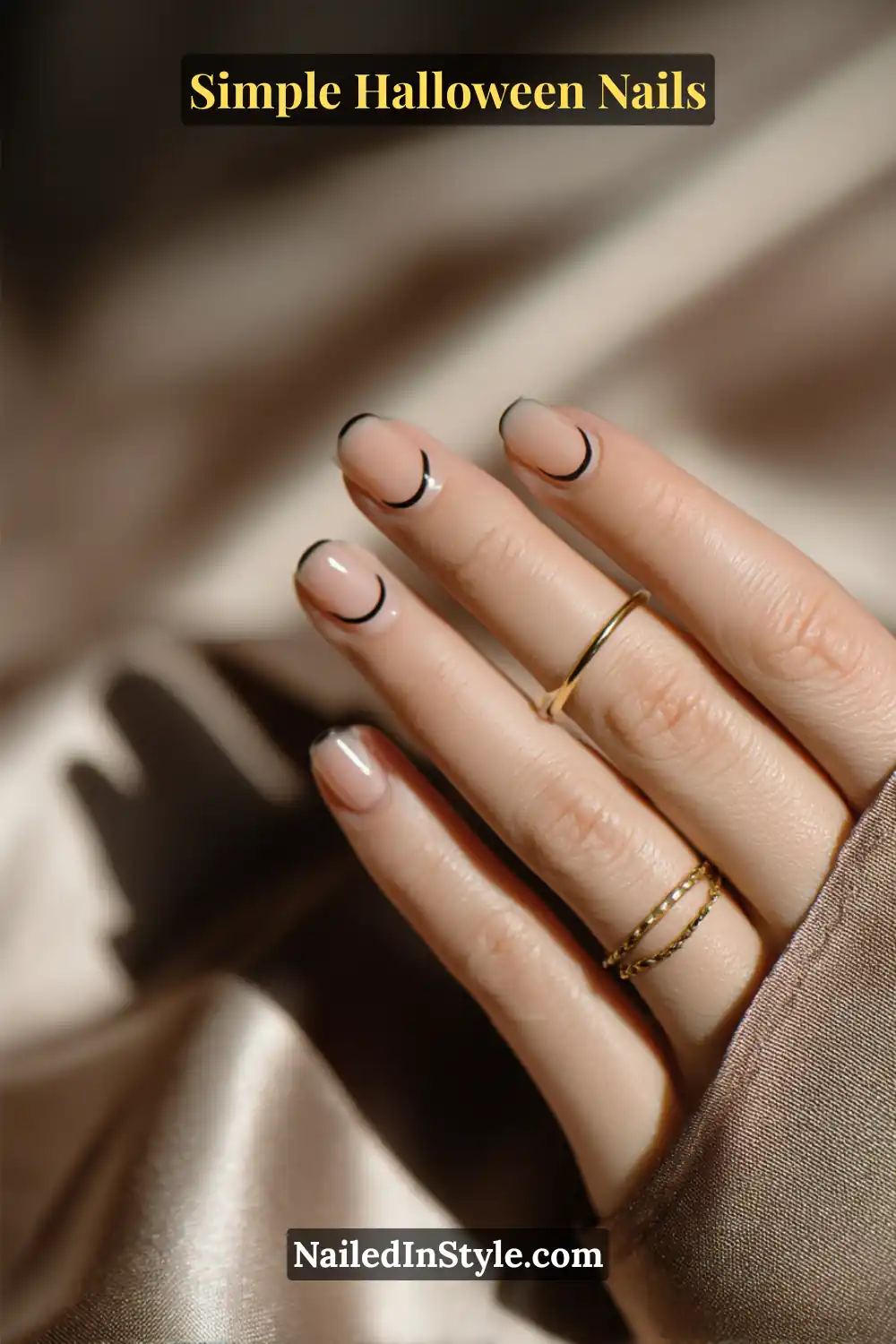 Simple Halloween Nails: Close-up of short squoval nails with a sheer latte base and ultra-thin black micro French tips; styled with gold rings and neutral satin background for a refined, minimalist Halloween nail look.
