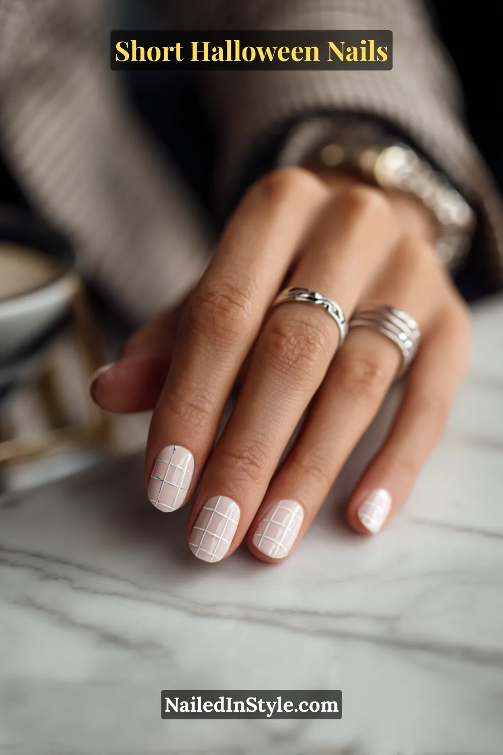 Short square nails with a porcelain base and fine white windowpane grid accent, clean and editorial look; styled with silver rings and a neutral blazer, modern Halloween nails for fair and medium skin tones.