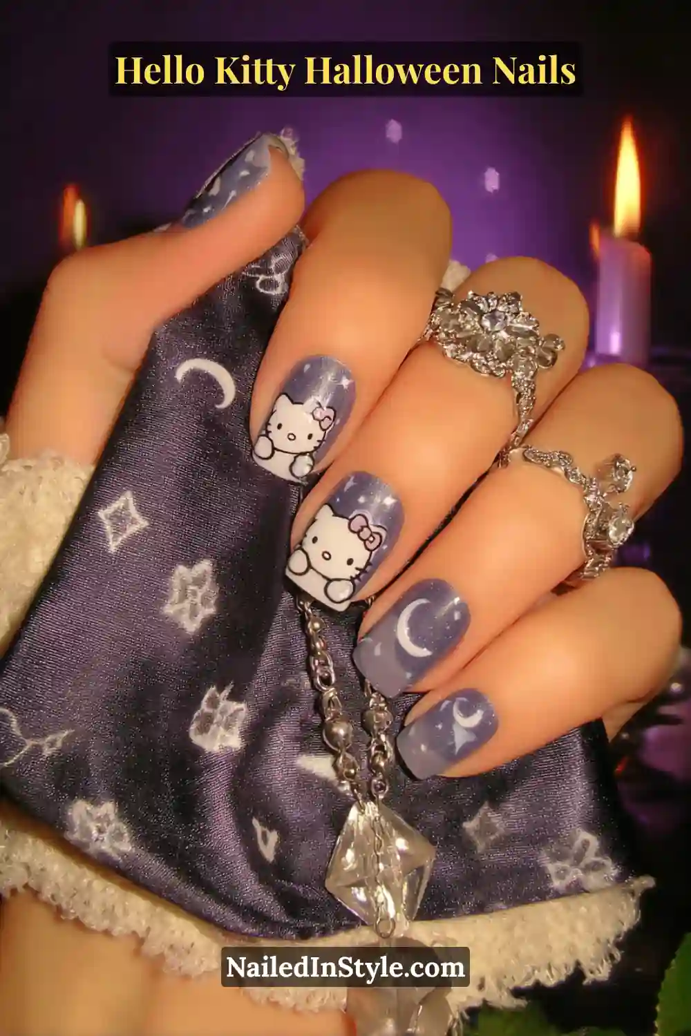 Medium almond nails in soft violet with 3D crescent moons and Hello Kitty outlines, featuring a smoky shimmer finish. Styled with silver crystal rings and a moon pendant for a dreamy Halloween vibe.