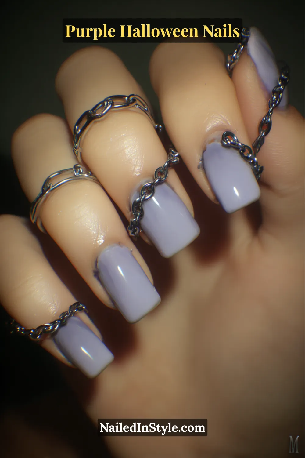 Short square nails painted in glossy lavender and accented with tiny pewter chain cuffs wrapping each fingertip — a 3D metallic detail that turns softness into statement.