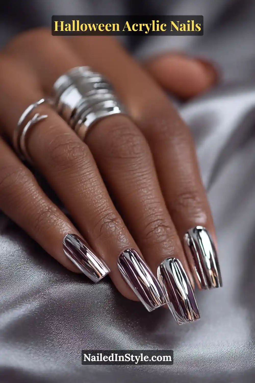Close-up of coffin-shaped acrylic nails featuring reflective mirror-chrome arcs resembling ribcage curves over a smoky jelly base, styled on deep skin tone with chunky silver rings and satin background.
