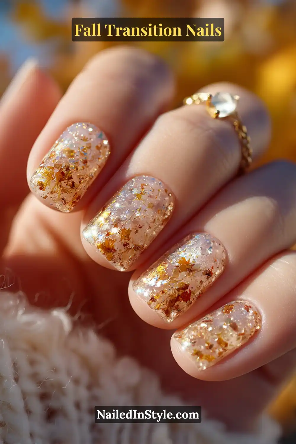 Short square nails with a glossy clear base filled with golden and maple-toned confetti flakes, glowing warmly under autumn sunlight.