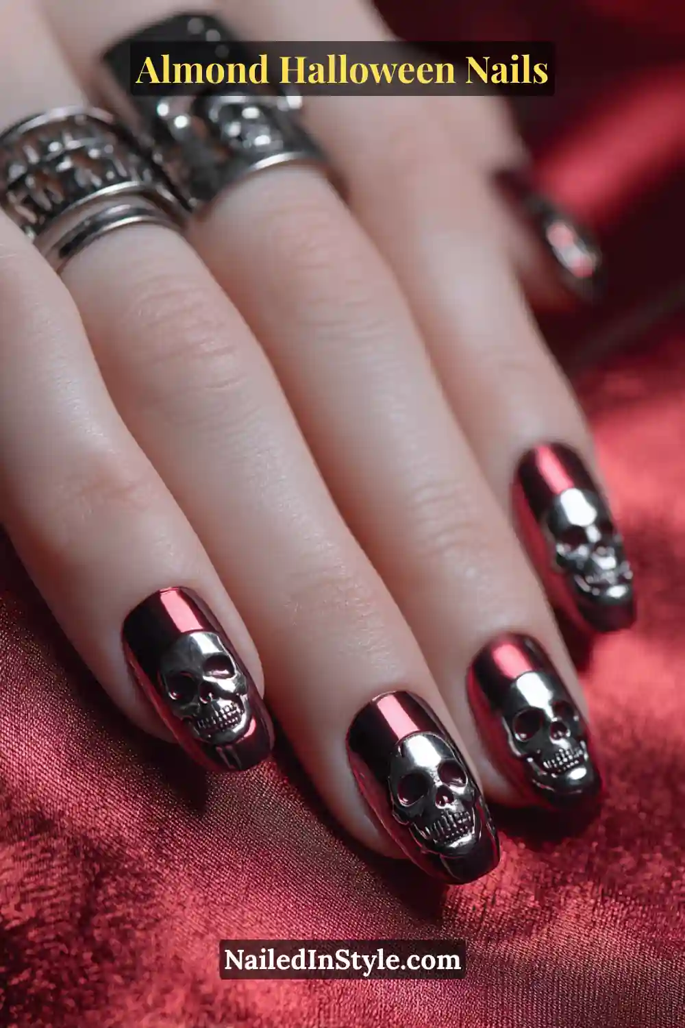 Close-up almond nails with red-to-black chrome fade and tiny silver skull emblems encapsulated at the center, high-shine metallic finish, Almond Halloween Nails.