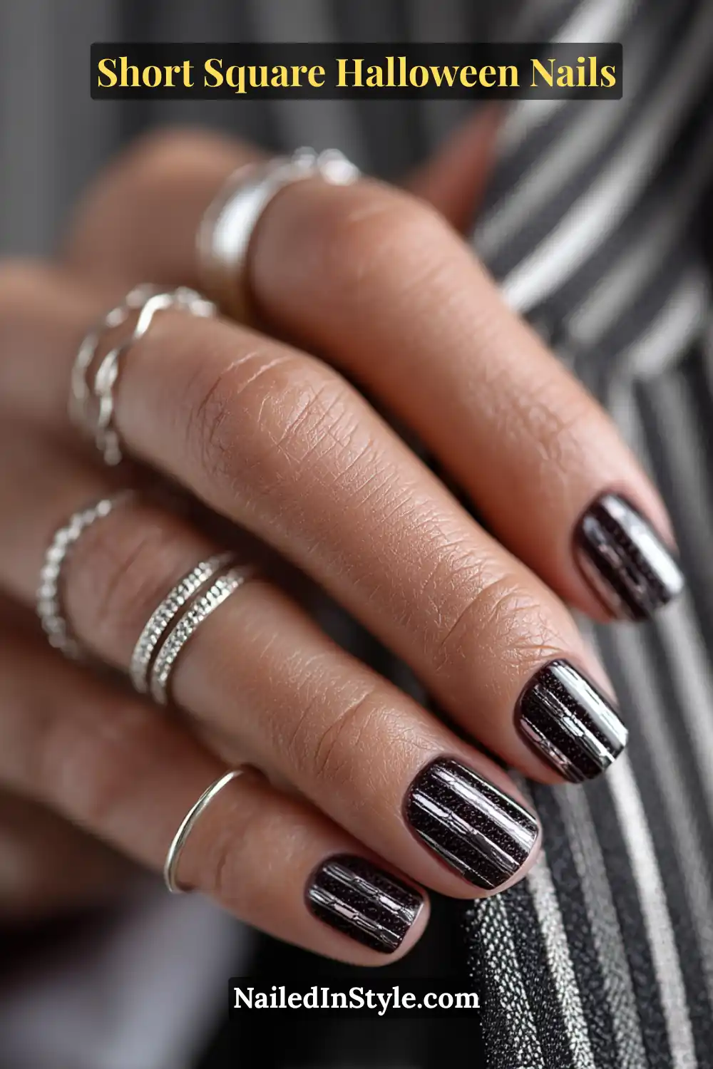 Short square nails in glossy black with vertical steel micro-stripes that create a barcode-inspired Halloween nail design.
