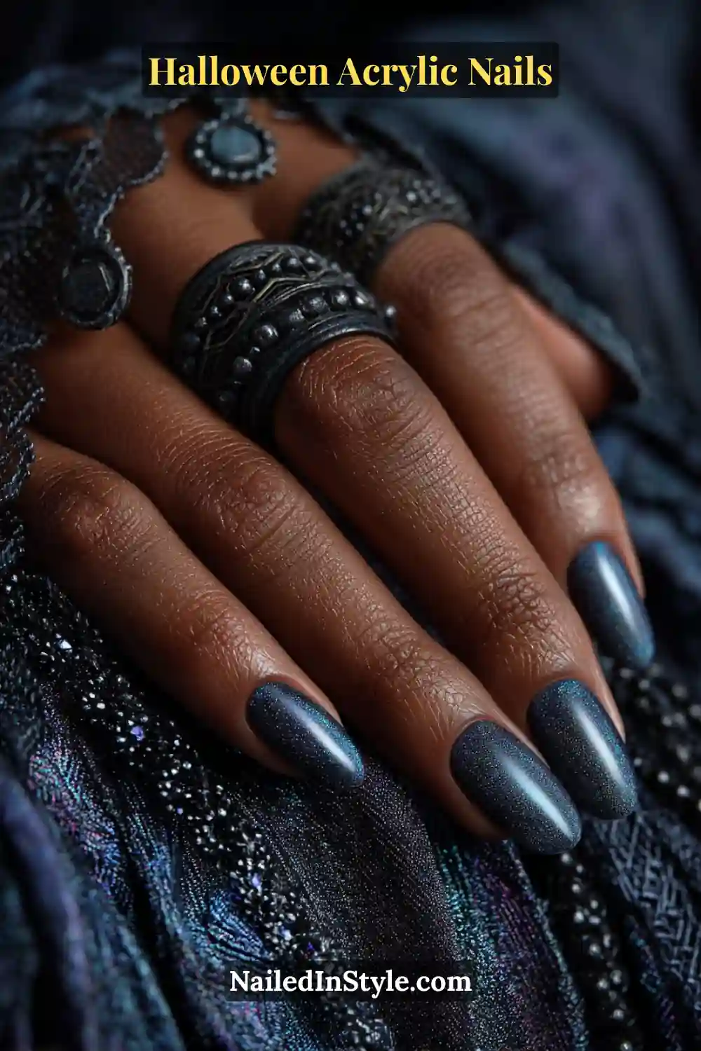 Close-up of almond-shaped Halloween acrylic nails in deep midnight blue shimmer resembling moth wings, styled with gothic silver rings and lace textures in dim lighting.