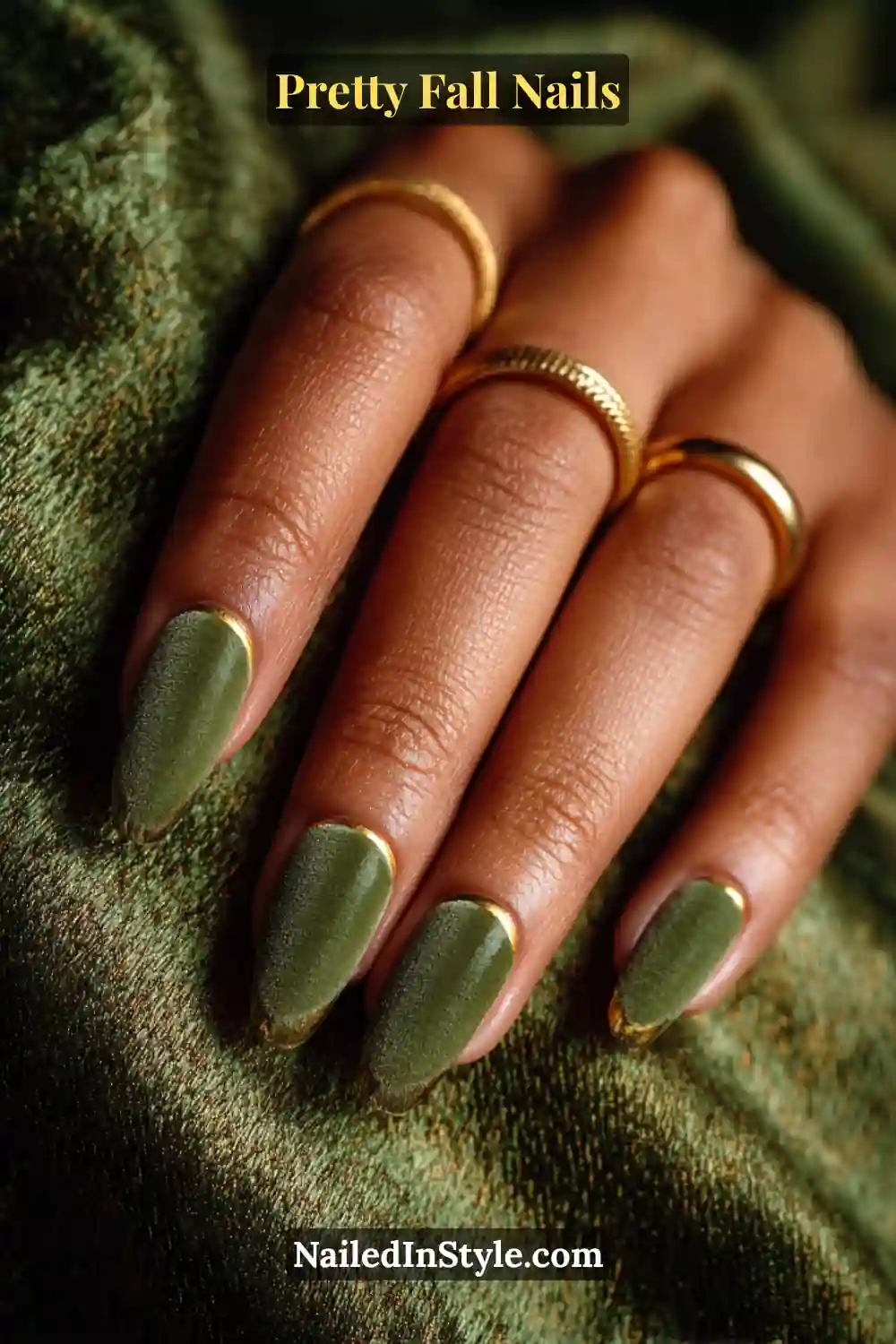 Long almond nails cloaked in deep moss-green velvet with slim metallic gold-lined tips, creating a lush, tactile French finish that radiates earthy elegance against golden skin tones.