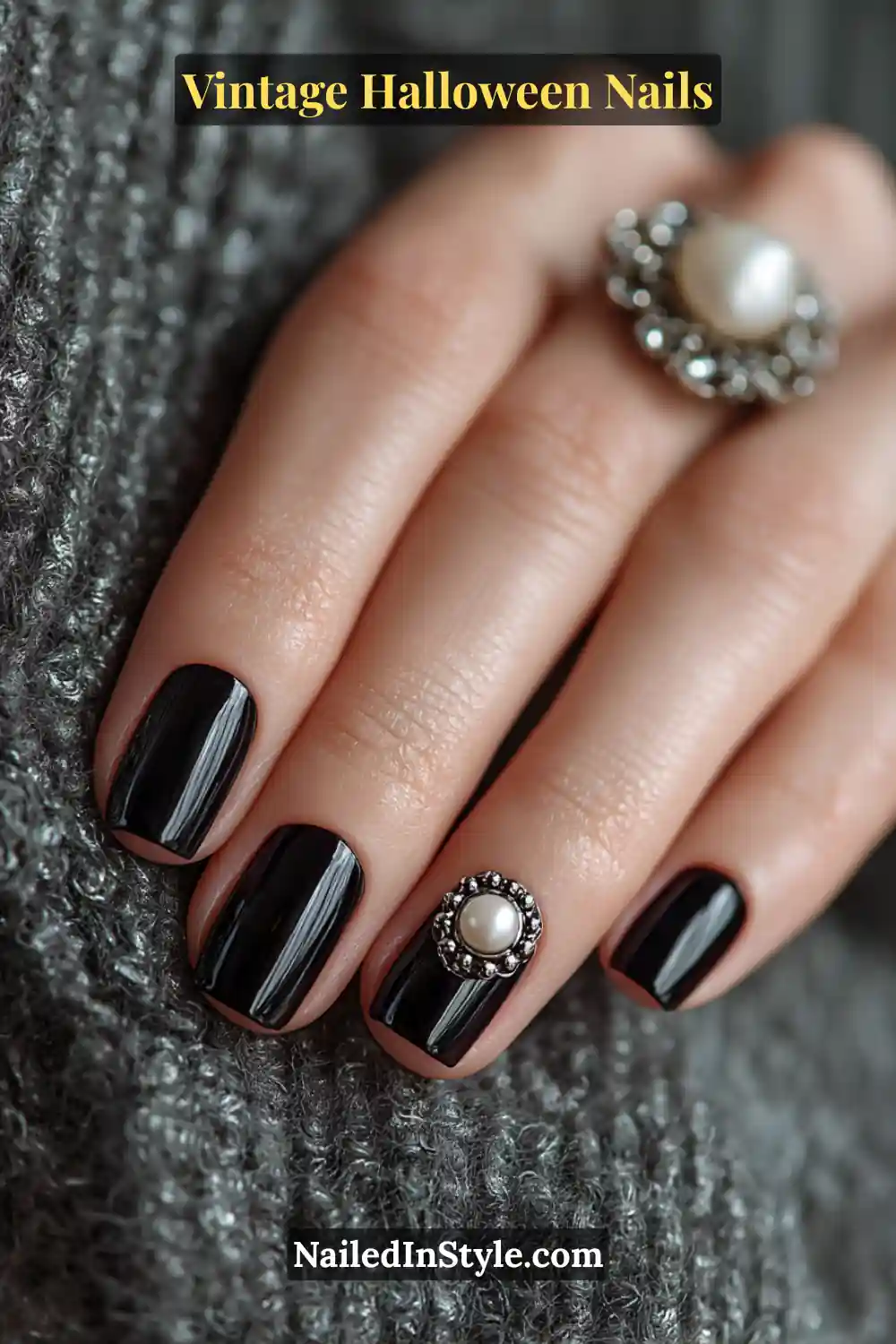 Short squoval nails in glossy jet black with a raised pearl brooch accent on one finger, adding a moody yet elegant 3D vintage Halloween charm.