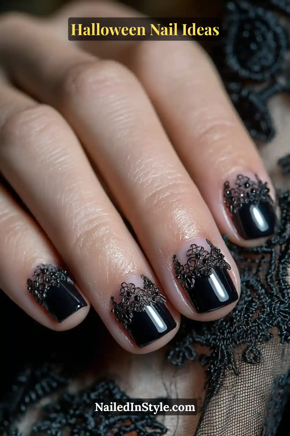 Short square nails featuring glossy jet-black tips with intricate lace-like cutout designs over a sheer blush base; paired with delicate black lace fabric for a gothic-chic Halloween aesthetic.