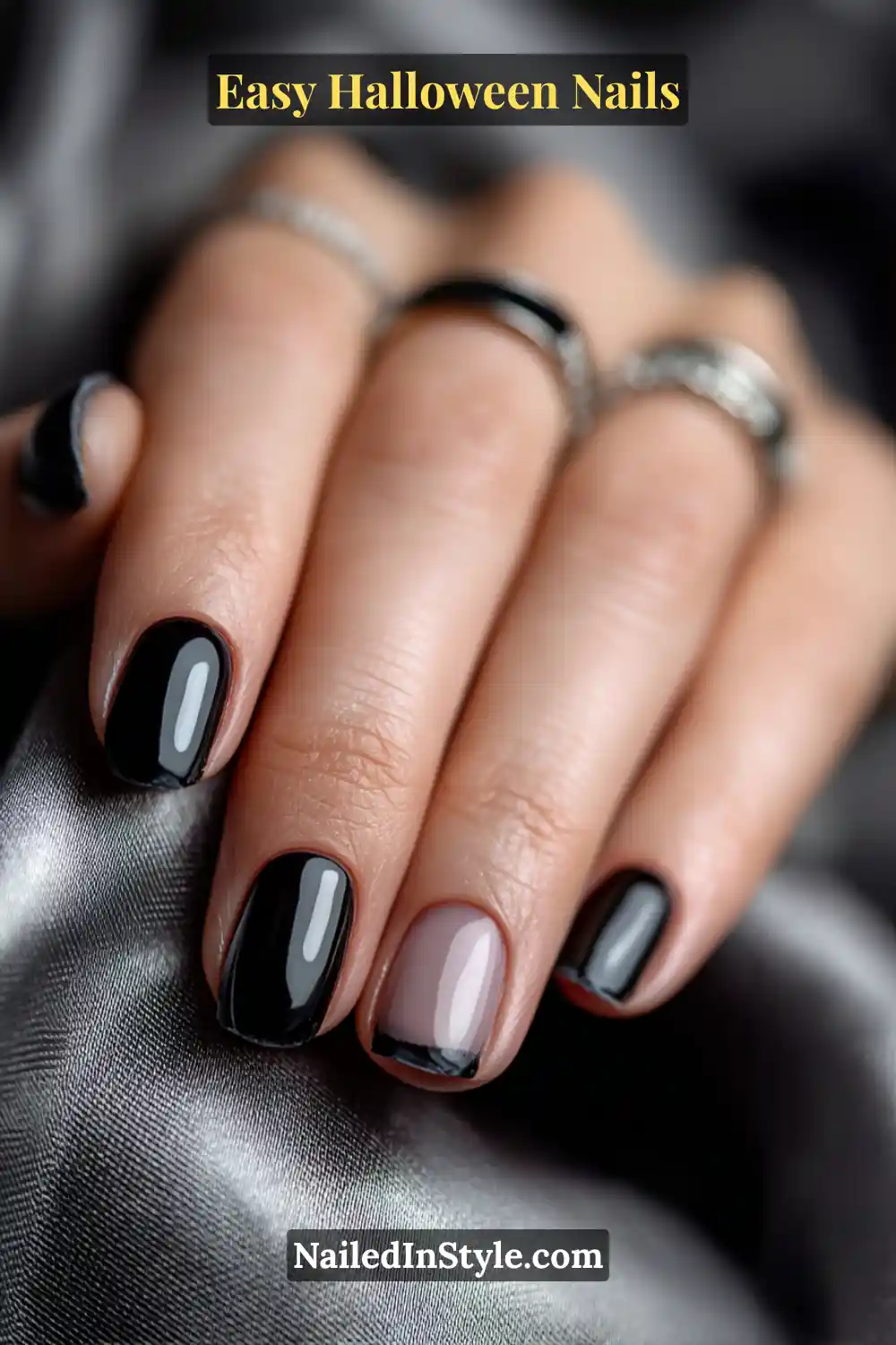 Short square nails featuring glossy black lacquer with one nail showing a sheer nude base and a fine black crescent edge, sleek and modern for Easy Halloween Nails.