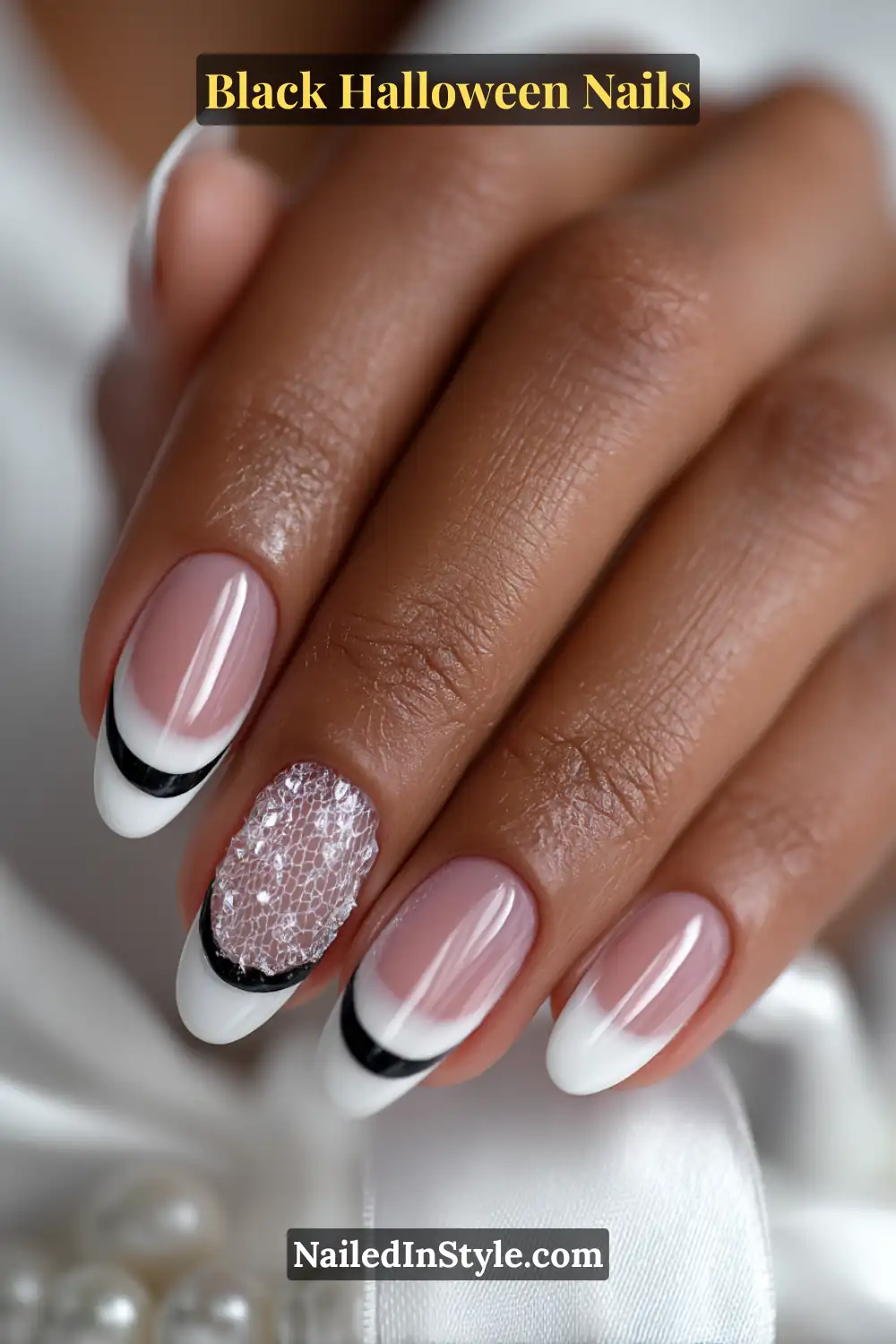 Medium almond nails in nude pink with ultra-thin black and white French tips, one accent nail featuring a delicate 3D heart-web design in silver; styled with satin fabric and pearl details.