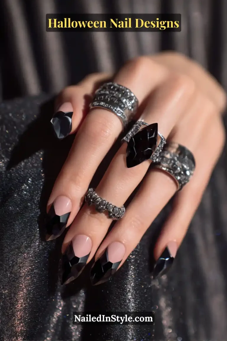 Close-up of almond nails with jagged onyx black shard-shaped tips and a glossy nude base, styled with chunky silver gemstone rings and metallic black fabric for a bold Halloween aesthetic.