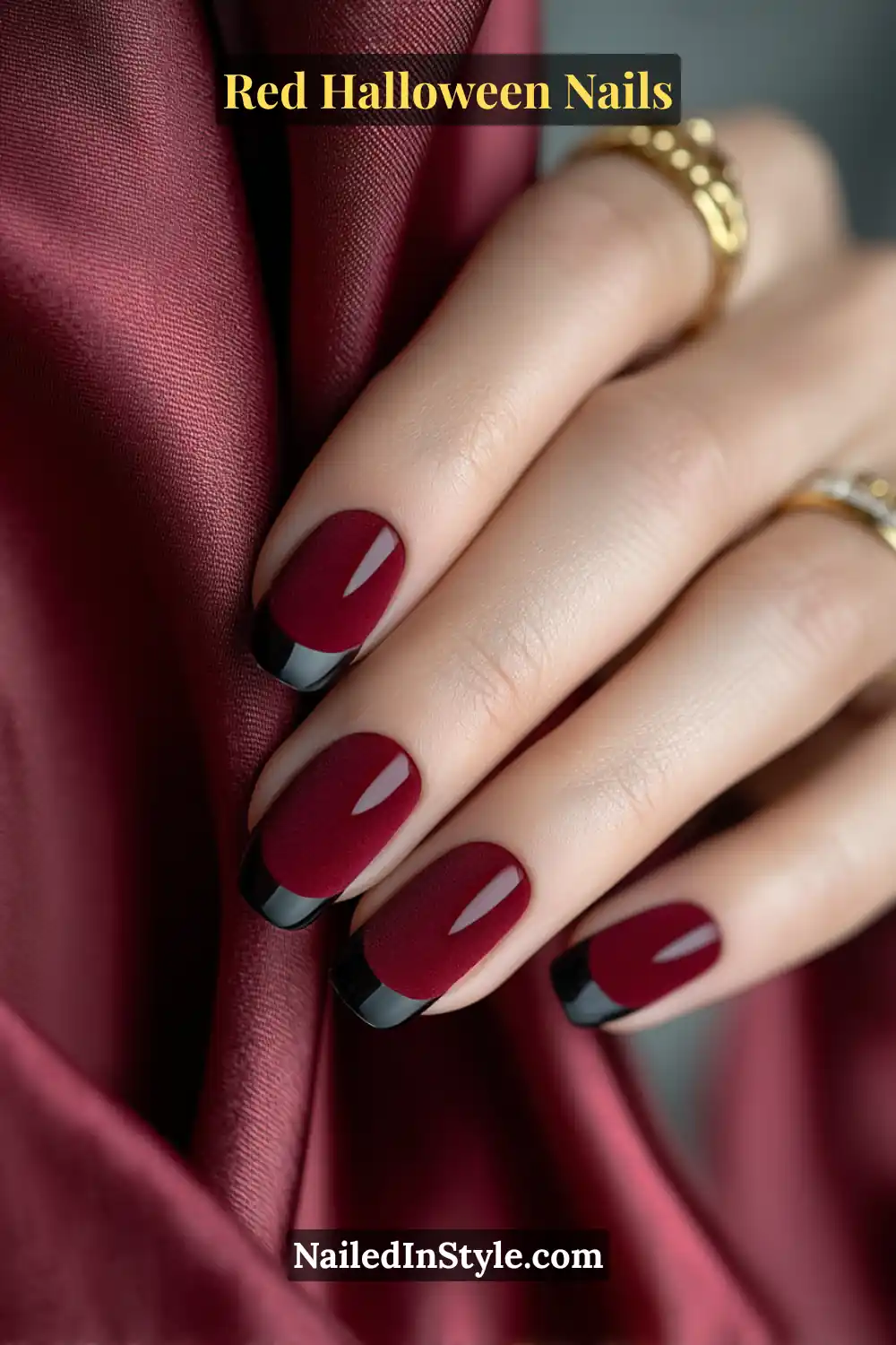 Close-up short squoval manicure in oxblood velvet matte with whisper-thin glossy black-cherry micro-French tips; gold signet ring and burgundy satin backdrop; flattering on fair–deep skin; luxe, spooky-glam vibe.
