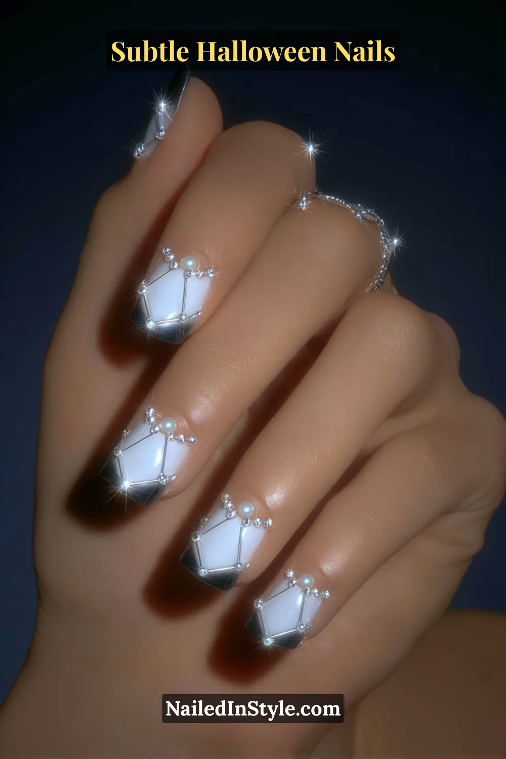 Short square nails with a translucent fog base, detailed by intricate 3D pearl web strands and silver micro accents that shimmer under soft light. The look is paired with a pearl clutch for a refined, celestial Halloween statement.