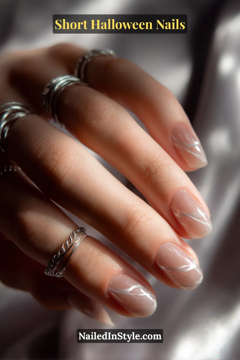 Close-up short oval nails with two translucent smoke stripes sweeping diagonally across a sheer nude base, leaving negative space between; styled with layered silver rings for a chic and ethereal Halloween nail look.