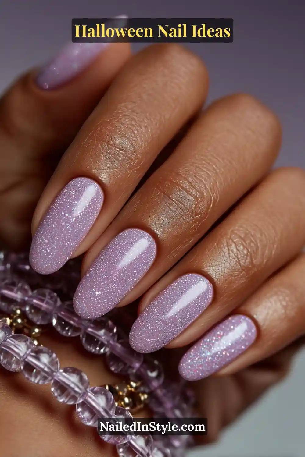 Short round nails in shimmering lilac smoke with delicate opal flake sparkle and 3D texture; styled with translucent glass-bead bracelets for a soft, magical Halloween glow.