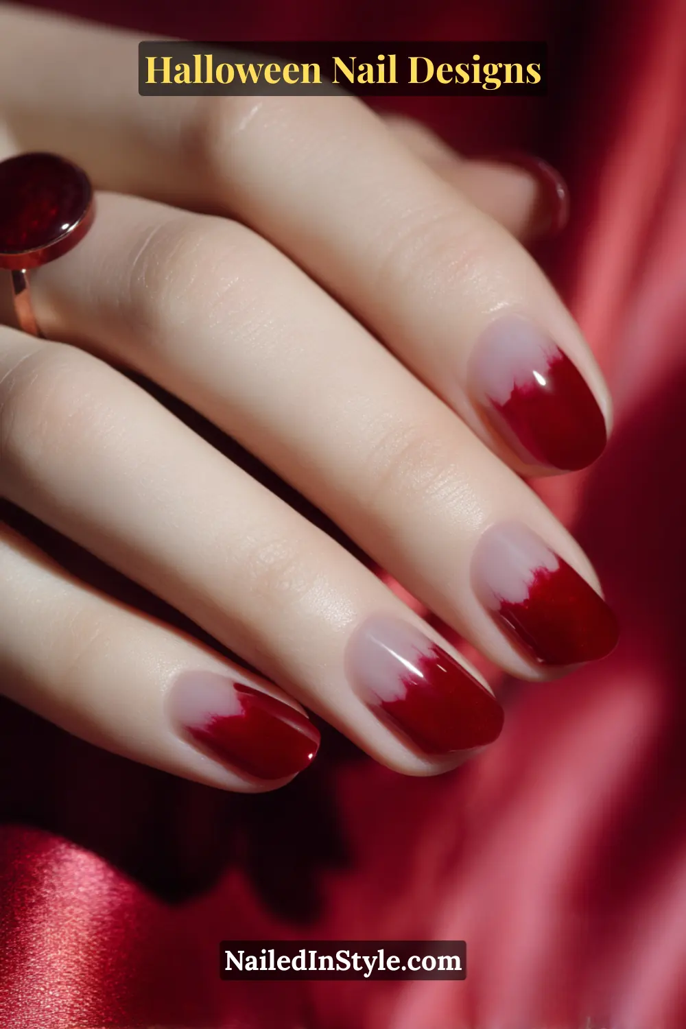 Close-up of oval nails featuring a reverse dip effect with glossy apple-red polish fading into a sheer nude base, styled on red satin fabric with a ruby ring.