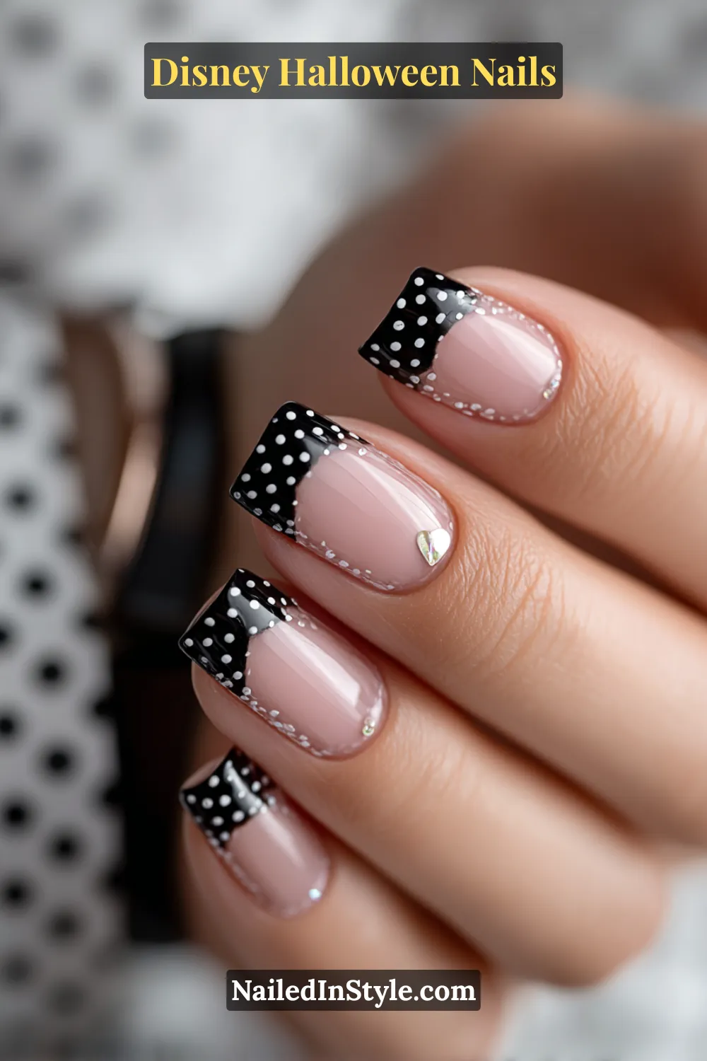 Extra-short square nails in glossy nude with jet-black French tips adorned by tiny white dots and a single silver heart accent; paired with a black watch strap for a playful yet chic Disney Halloween vibe.