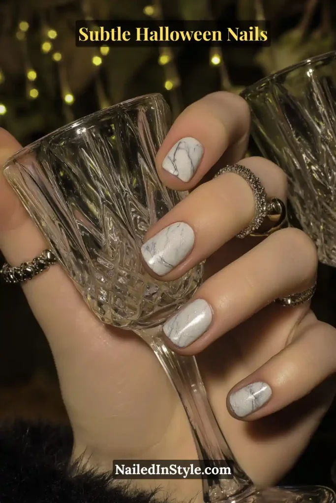 Short round nails with a sheer porcelain base softly veined in smoke-gray marbling, creating a ghostly, translucent effect that feels both clean and mysterious. Styled with a crystal tumbler to enhance the ethereal Halloween mood.