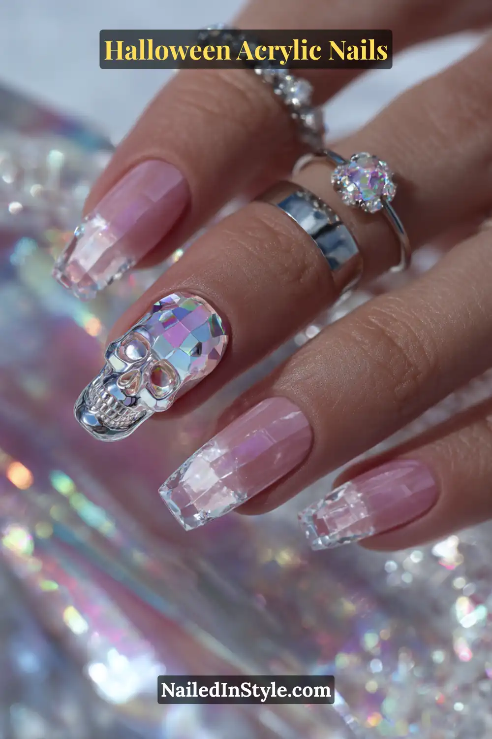 Close-up of coffin-shaped acrylic nails featuring crystal-clear tips with holographic prism facets and an opal-amethyst skull encapsulated at the center, surrounded by metallic rings and iridescent lighting.