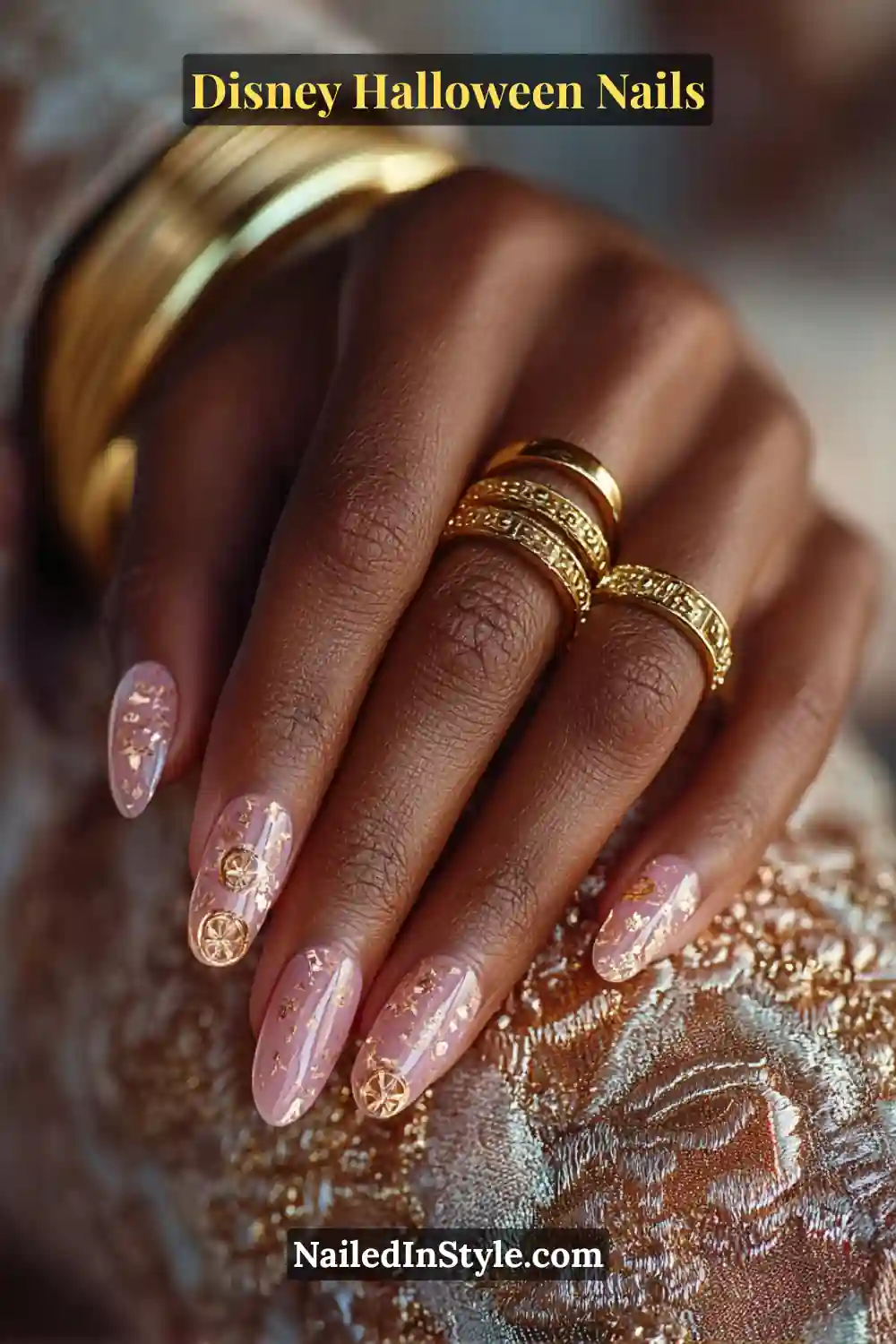 Long almond nails in sheer peach jelly with delicate gold foil and tiny 3D carriage-wheel accents; paired with ornate gold bangles for a glowing Disney princess look.