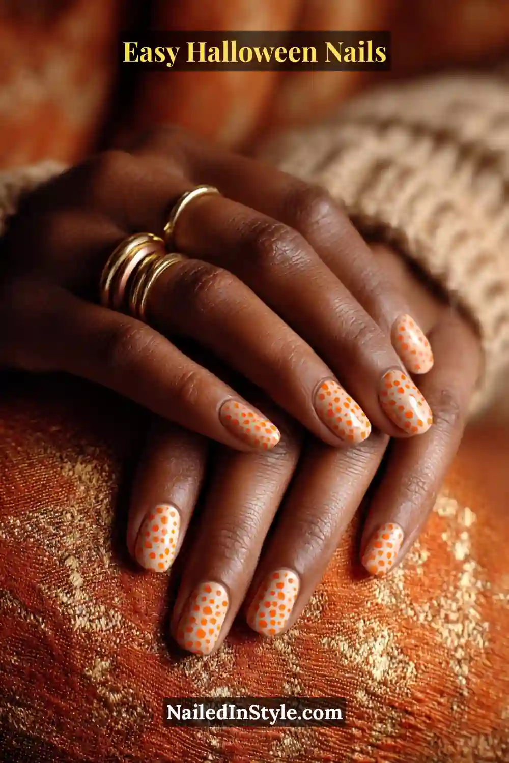 Almond nails painted with a soft neutral base and pumpkin-orange dots forming half-moon shapes near the cuticle, finished with a satin glow for Easy Halloween Nails.