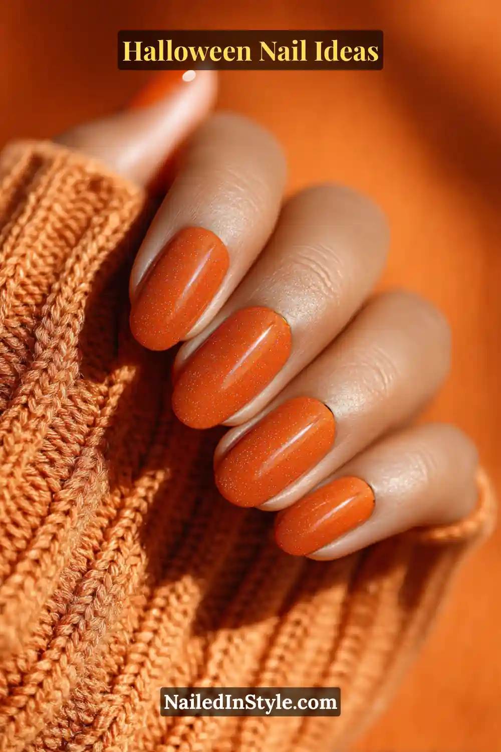 Medium almond nails in glowing pumpkin orange with a soft latte undertone and subtle halo effect; a tiny raised chrome dot at each apex catches the light, paired with a cozy knit sleeve for an autumn-inspired look.