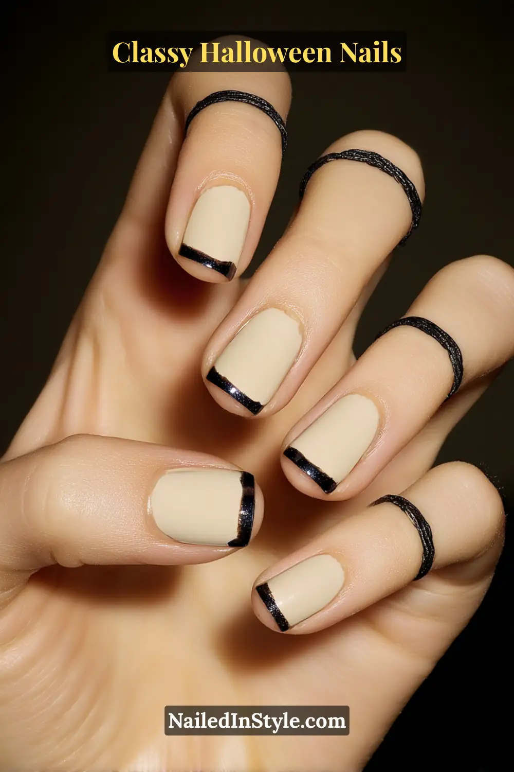 Short square nails in soft pearl beige with razor-thin glossy black French tips — a modern ribbon-edge design that defines elegance with subtle Halloween charm.