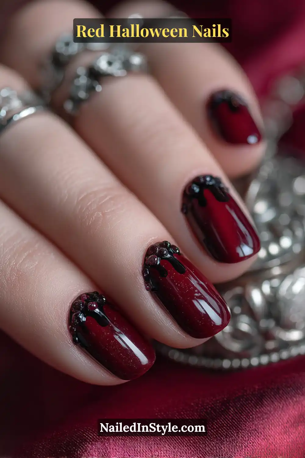 Short square nails in glossy ruby red with sculpted black drip domes near the cuticle; playful 3D texture adds Halloween charm; complemented by silver rings and a dark satin background; suits all skin tones for a bold yet wearable spooky look.
