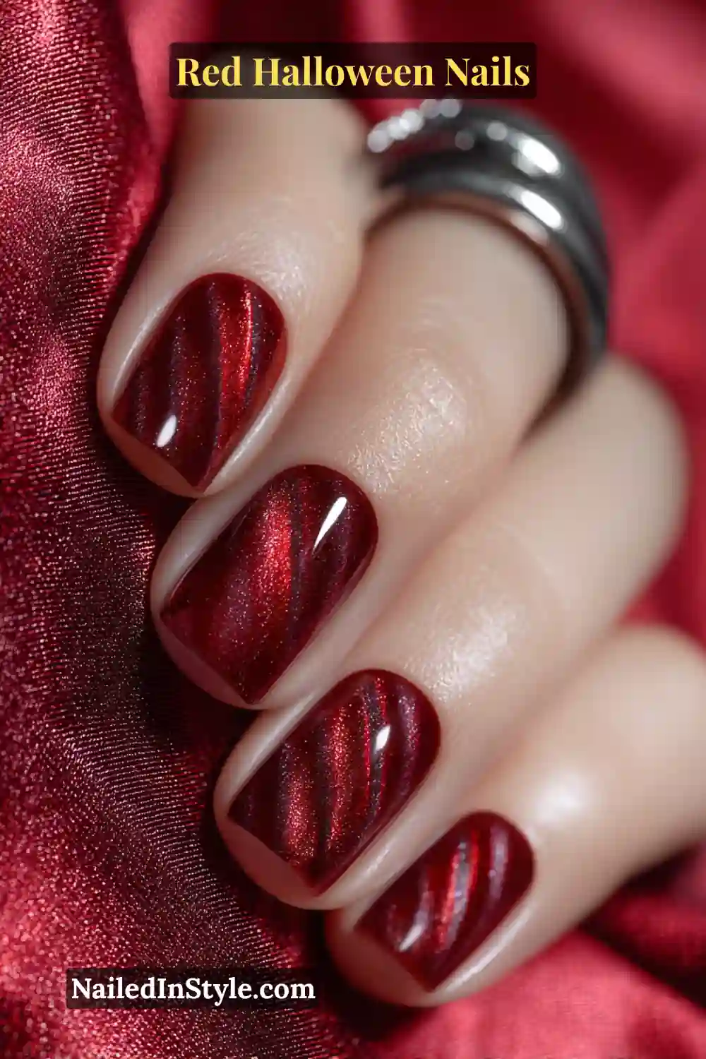 Short square nails in magnetic scarlet red with a diagonal cat-eye beam and thin soot-black outline; luminous light-reflecting finish paired with silver gunmetal jewelry; flattering on all skin tones for a fiery, shifting effect.