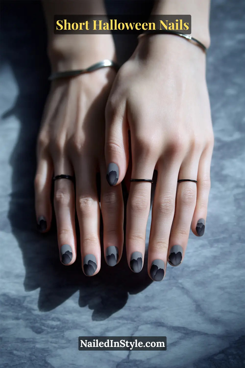 Short oval nails featuring soft charcoal petal silhouettes clustered near one sidewall for a romantic shadowed effect; styled with minimalist silver and black rings, elegant short Halloween nails for all skin tones.