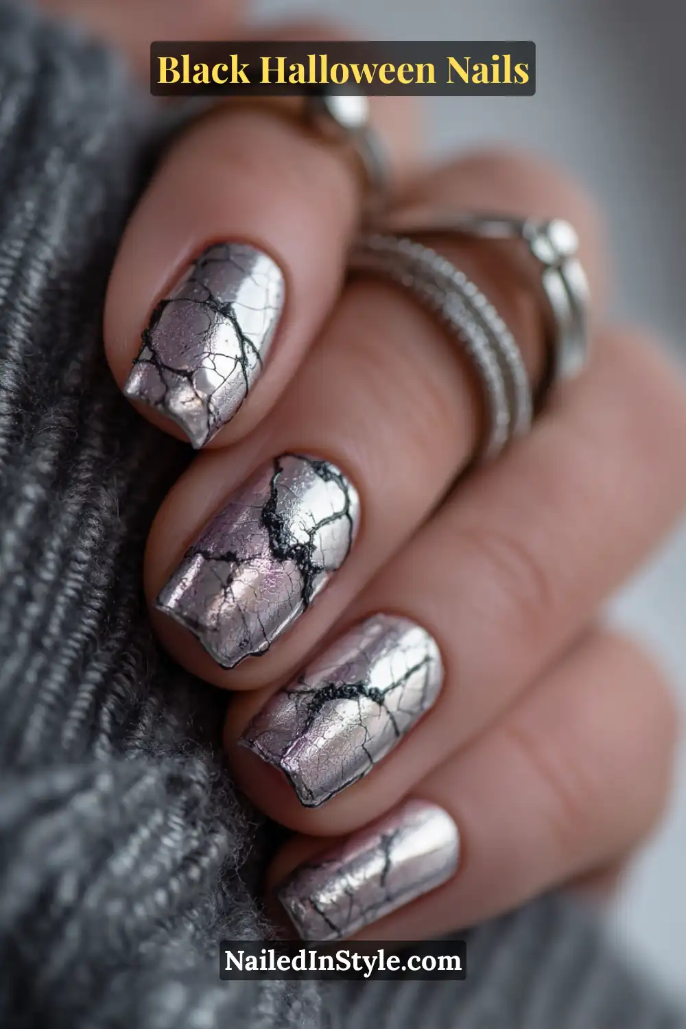 Black Halloween Nails Medium square nails featuring a metallic silver base with faint raised black heart-web details and a 3D silver cuff accent; styled with stainless stacked rings and cozy gray knitwear.