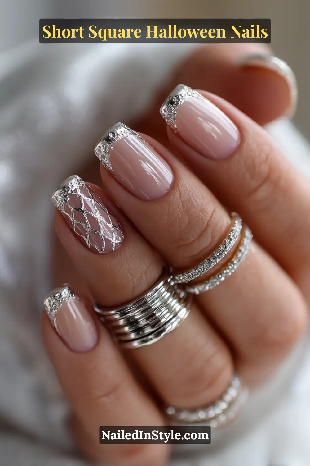 Short square nude nails with metallic silver cuffs and delicate web lattice detailing, finished with a glossy Halloween-inspired shine.