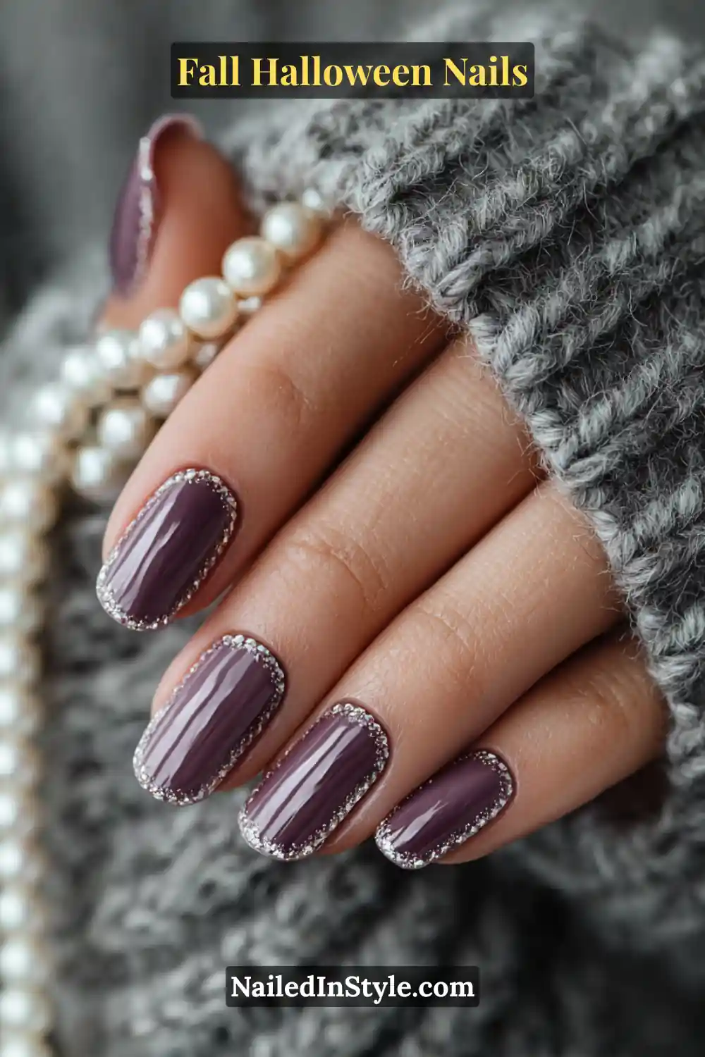 Short squoval nails in deep amethyst tones framed with a fine pearl outline, styled beside a gray knit sleeve and a strand of pearls for a sophisticated autumn-luxe mood.
