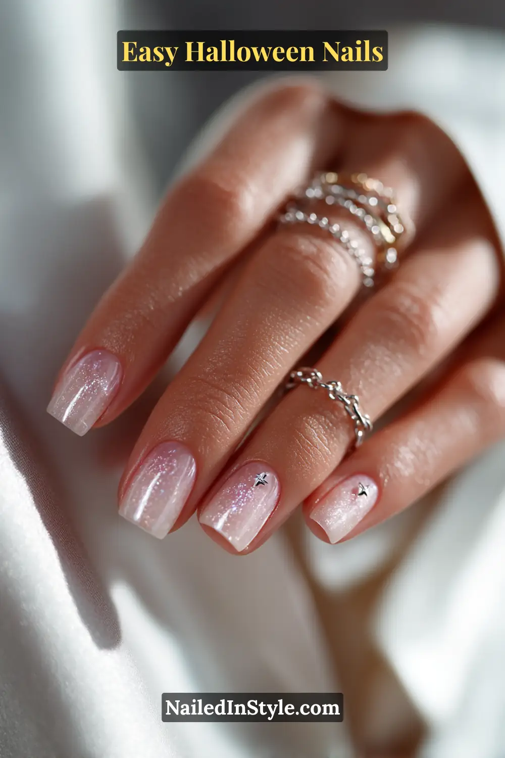 Short square nails with a sheer pink base and two tiny sterling silver star accents near the cuticle, finished with a glossy shimmer effect for Easy Halloween Nails.